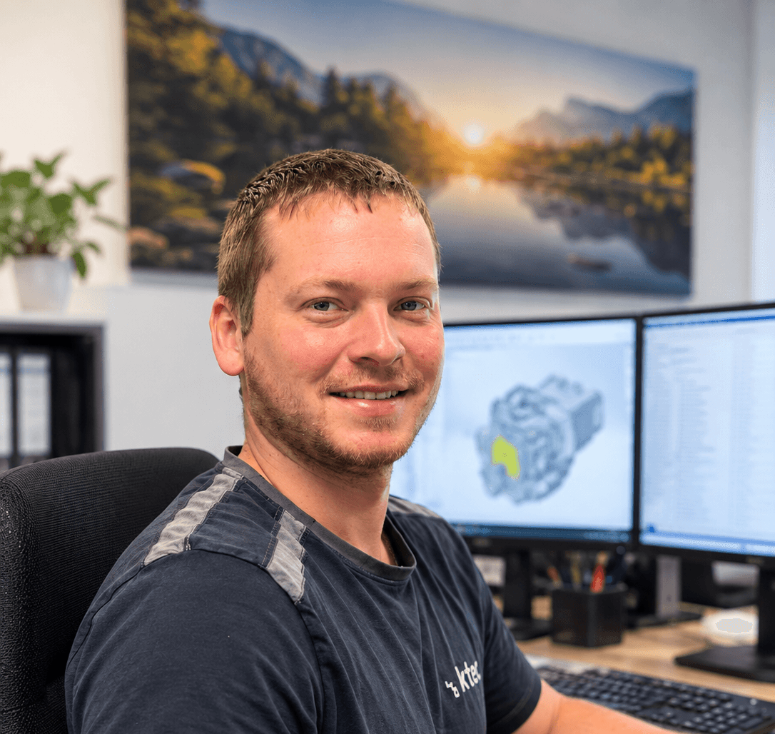 Martin Prechtl, Leiter Zerspanung bei RK-tec, sitzt lächelnd am Schreibtisch, im Hintergrund CAD-Modell auf zwei Monitoren